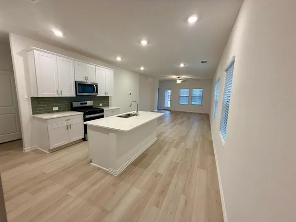 a large white kitchen with stainless steel appliances granite countertop a stove a sink dishwasher and a microwave with wooden floor