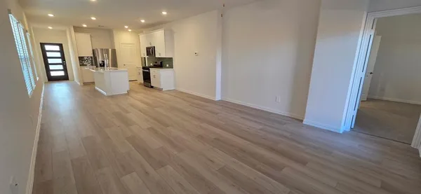 a view of an empty room and kitchen with wooden floor