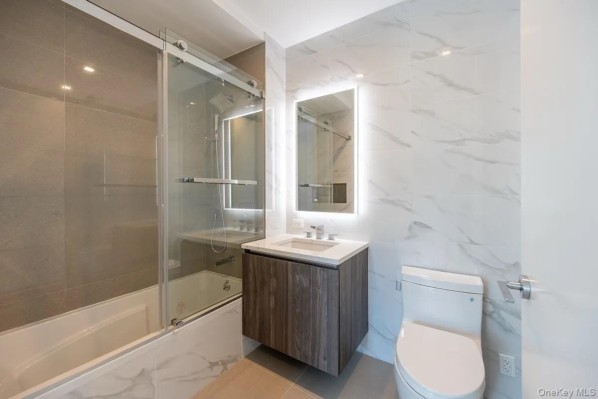 33-66 Farrington Street, Unit 9K Queens, NY 11354 - Photo 5 of 9 Bathroom featuring bath / shower combo with glass door, vanity, tile walls, and light tile patterned floors