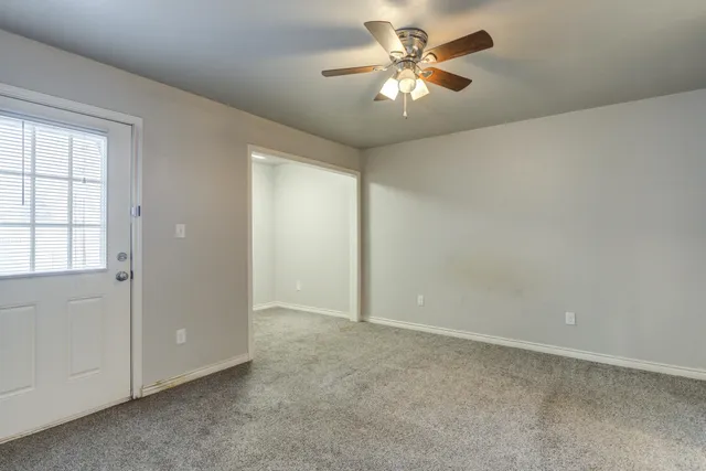 an empty room with chandelier fan and windows