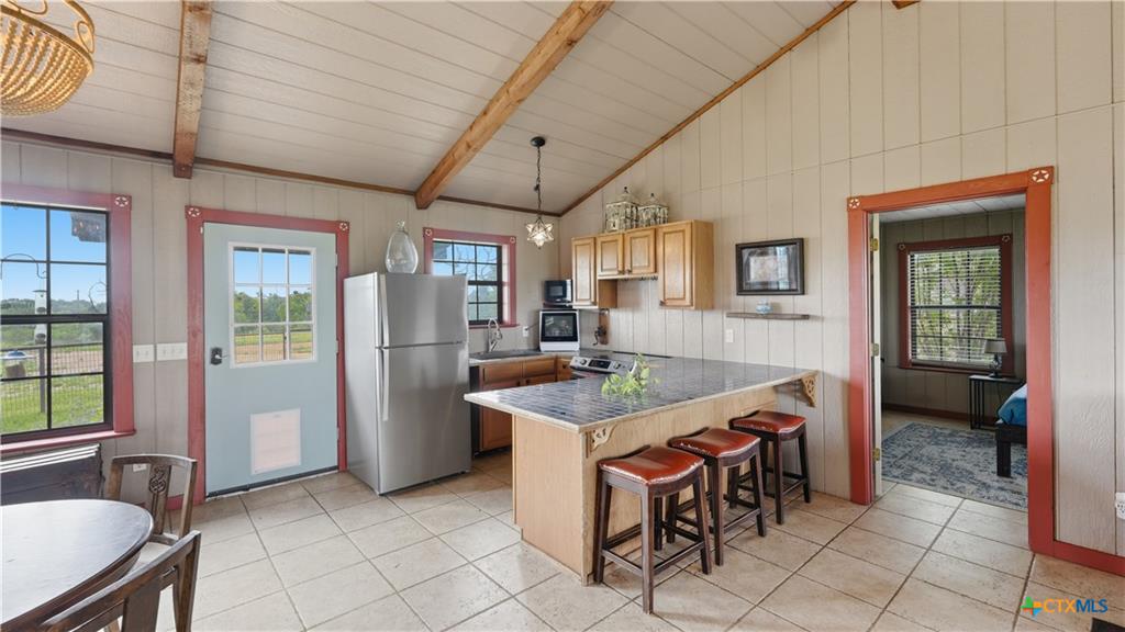 127 Offer Llano, TX 78643 - Photo 4 of 40 Kitchen with tile flooring featuring exposed wood ceiling beams, a central island with bar seating, wood cabinetry, and stainless steel appliances
