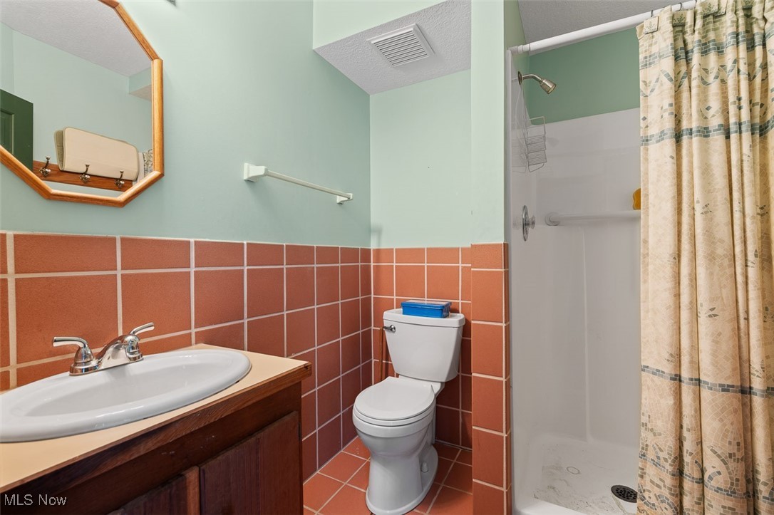 256 Everhard Road Southwest North Canton, OH 44709 - Photo 15 of 45 Full bath featuring a shower stall, tile walls, vanity, tile patterned flooring, and a wainscoted wall