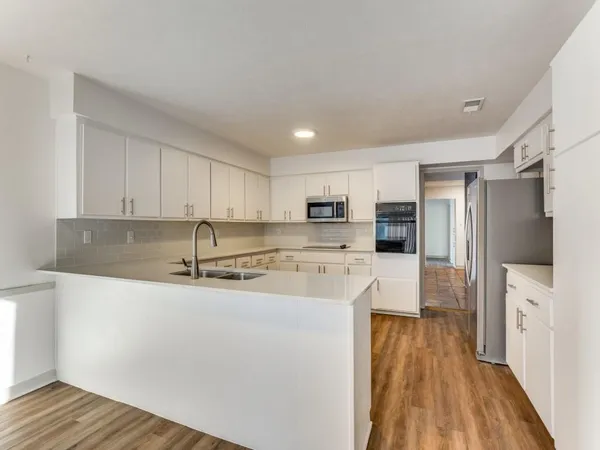 a large kitchen with stainless steel appliances granite countertop a refrigerator a stove a sink and white cabinets with wooden floor