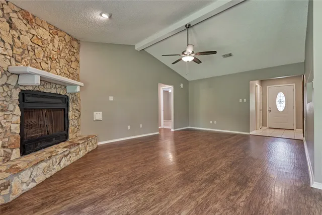 an empty room with wooden floor a ceiling fan a fireplace and windows