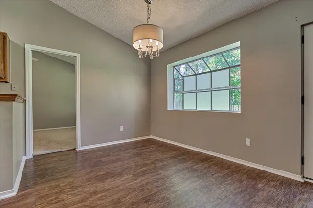 an empty room with wooden floor chandelier and windows