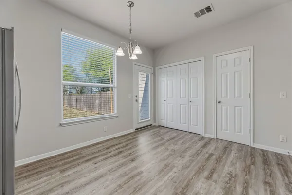 an empty room with wooden floor chandelier and windows