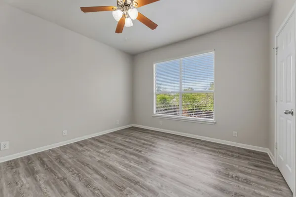 an empty room with wooden floor fan and windows