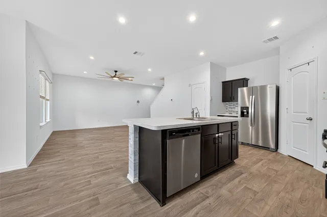 a large kitchen with stainless steel appliances a large counter top a stove a refrigerator cabinets and a wooden floor