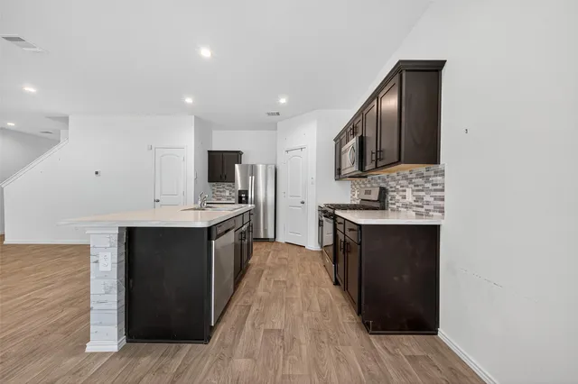 a large kitchen with stainless steel appliances granite countertop a stove top oven a sink and dishwasher with wooden floor