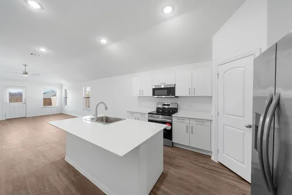 a kitchen with stainless steel appliances a sink stove refrigerator and white cabinets with wooden floor