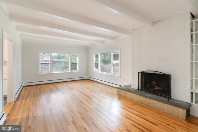 an empty room with wooden floor fire place and windows