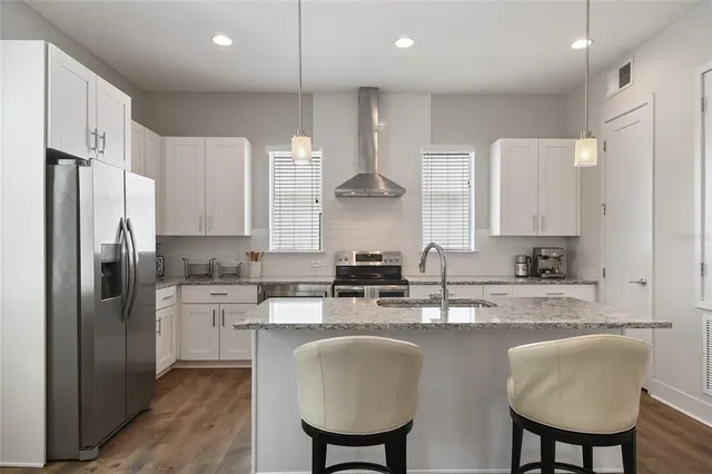 a kitchen with stainless steel appliances granite countertop a kitchen island a stove a sink a refrigerator and white cabinets