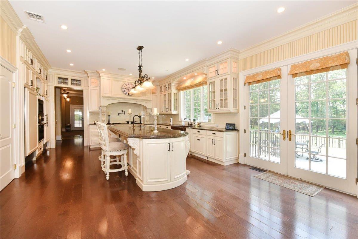 1616 Stewart Lane Syosset, NY 11791 - Photo 17 of 38 Kitchen featuring french doors, a center island with sink, a kitchen bar, ornamental molding, and glass insert cabinets