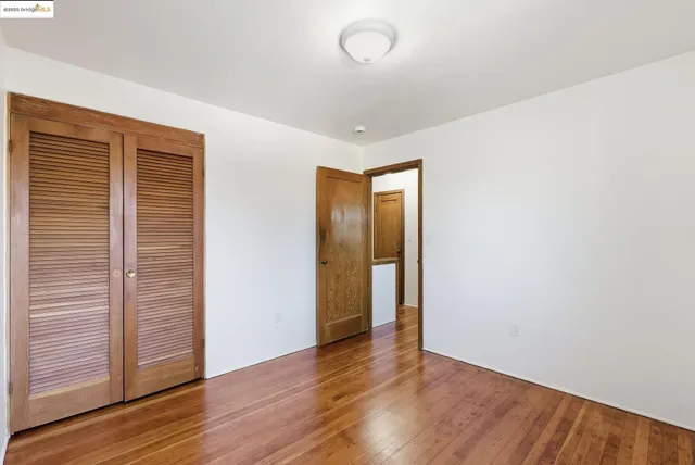 a view of an empty room with wooden floor and closet
