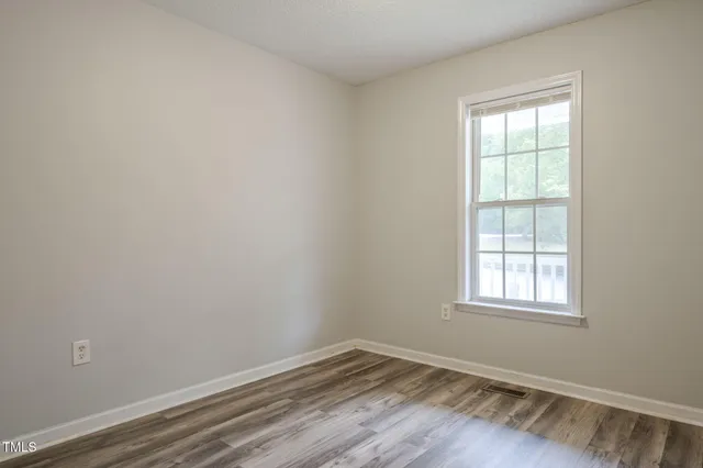an empty room with wooden floor cabinet and windows