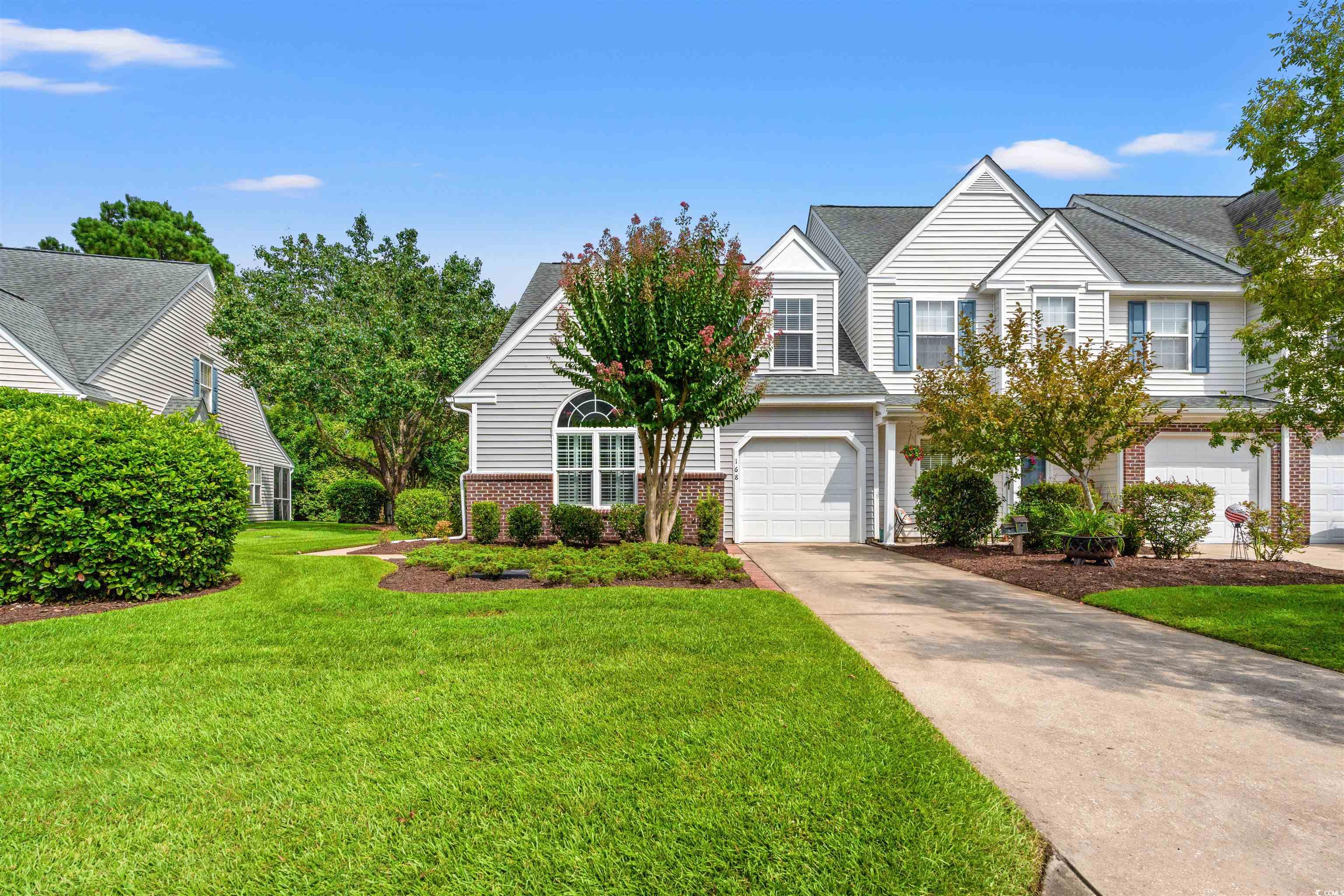 Traditional-style house featuring concrete driveway, a front lawn, an attached garage, and roof with shingles