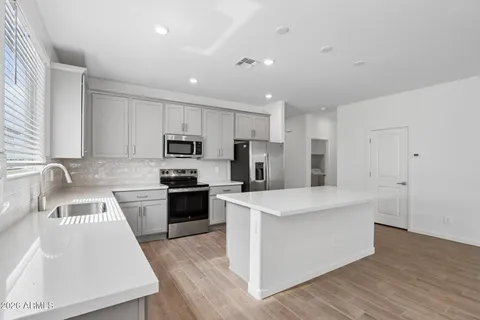 a kitchen with stainless steel appliances granite countertop a stove top oven a sink a refrigerator white cabinets and wooden floor