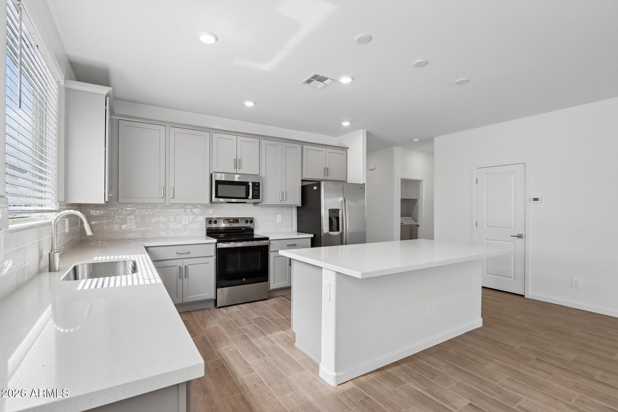 9544 West Gaby Road Tolleson, AZ 85353 - Photo 9 of 43 a kitchen with stainless steel appliances granite countertop a stove top oven a sink a refrigerator white cabinets and wooden floor