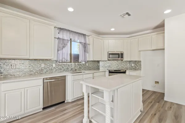 a kitchen with stainless steel appliances granite countertop a stove top oven a sink a refrigerator white cabinets and wooden floor