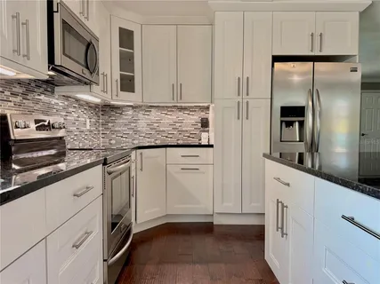 a kitchen with stainless steel appliances granite countertop a sink a stove a refrigerator cabinets and a dining table with wooden floor