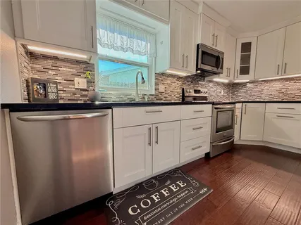 a open kitchen with stainless steel appliances granite countertop a refrigerator a stove a microwave oven a stove and white cabinets with wooden floor