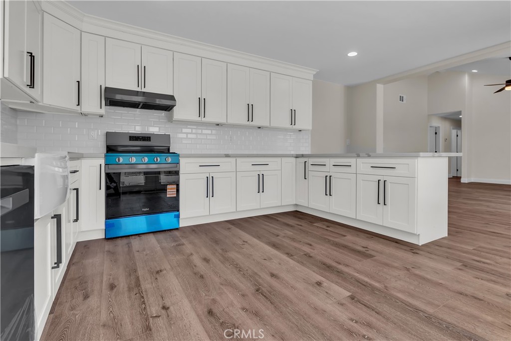 a kitchen with stainless steel appliances granite countertop a stove top oven a sink dishwasher and a refrigerator with wooden floor