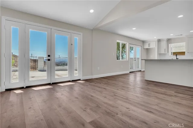 a view of empty room with wooden floor and kitchen