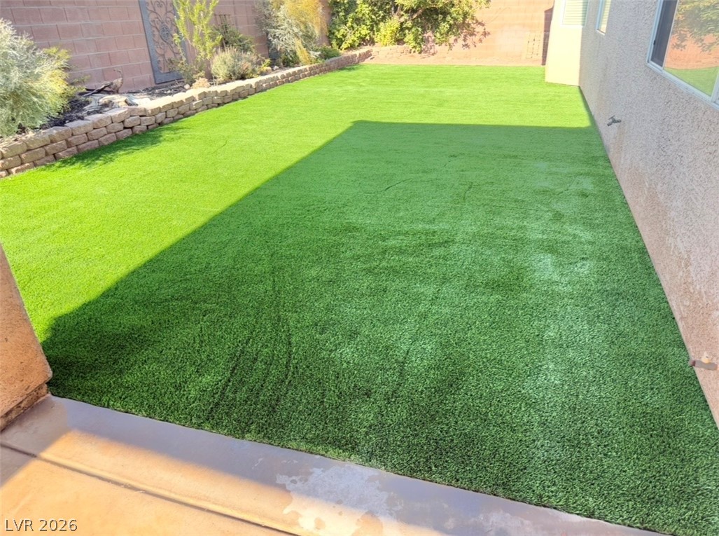 9996 Liberty View Road Las Vegas, NV 89148 - Photo 66 of 66 Green artificial turf creates a vibrant, low-maintenance outdoor space bordered by a stone retaining wall and mature plantings.