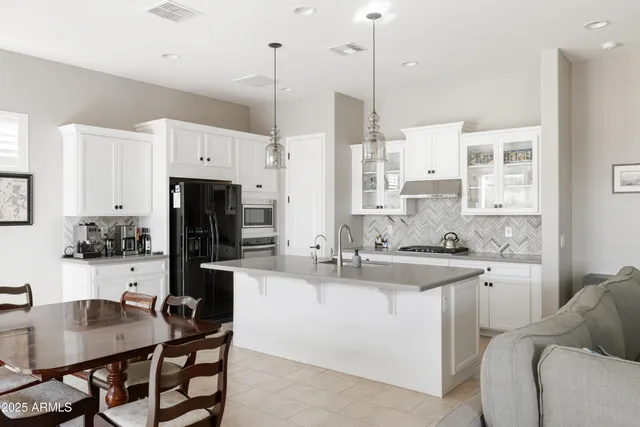 a kitchen with stainless steel appliances kitchen island granite countertop a sink a stove a refrigerator and white cabinets with wooden floor