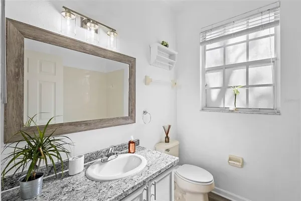 a bathroom with a granite countertop sink a toilet a mirror and a window