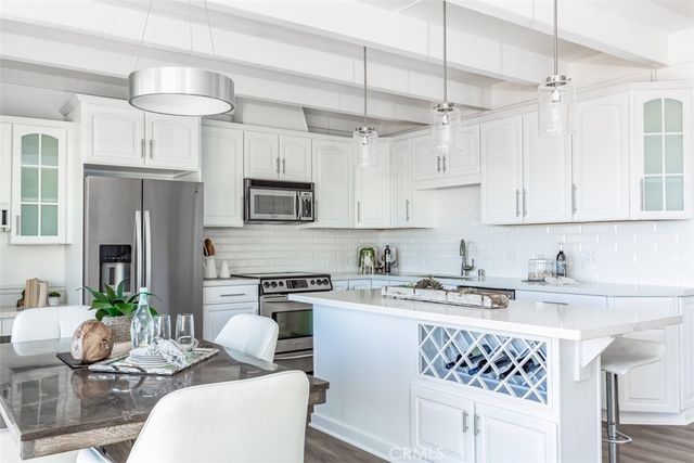 a kitchen with stainless steel appliances kitchen island granite countertop a refrigerator a stove a sink dishwasher a dining table and chairs with wooden floor