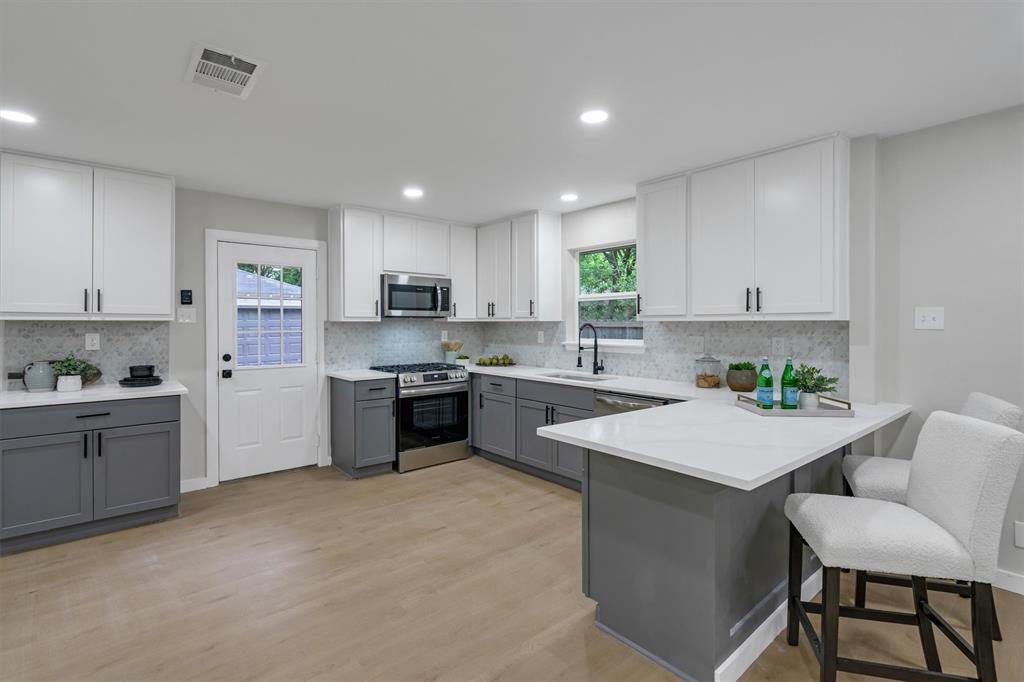 4815 Kelman Street Dallas, TX 75214 - Photo 16 of 37 Modern kitchen featuring two-tone cabinetry with matte black hardware, stainless steel appliances, a white tile backsplash, and light wood-finish flooring