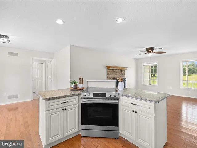 a view of an empty room and kitchen with fireplace ceiling fan