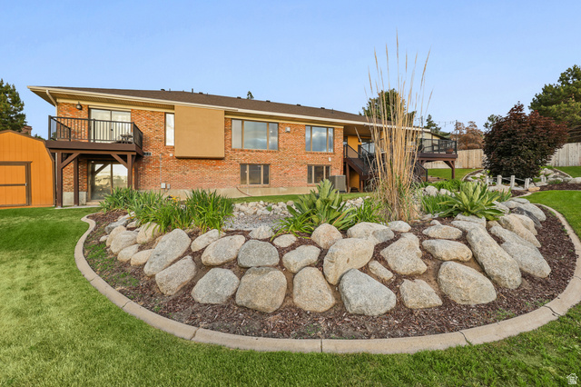 2342 Charros Road Sandy, UT 84092 - Photo 92 of 94 Expansive backyard featuring a manicured lawn, a large stone-edged garden bed with varied plantings, and a red brick exterior