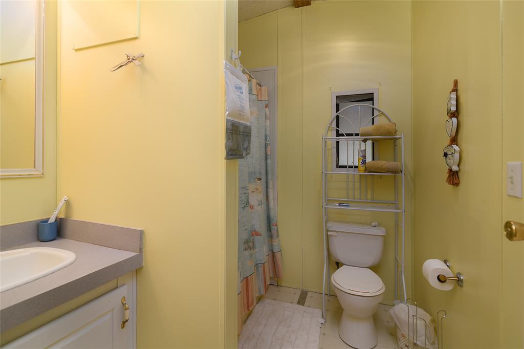 122 Grice Road Ringgold, LA 71068 - Photo 16 of 26 Bathroom featuring a light-colored vanity with a white basin and gray countertop, a white toilet with an open metal shelving unit, and a shower area with a patterned curtain