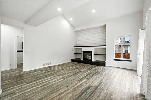 an empty room with wooden floor fireplace and windows