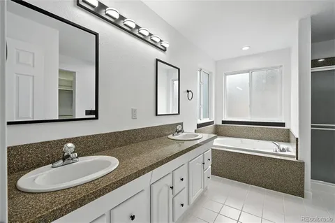 a bathroom with a granite countertop double vanity sink a mirror and a bathtub