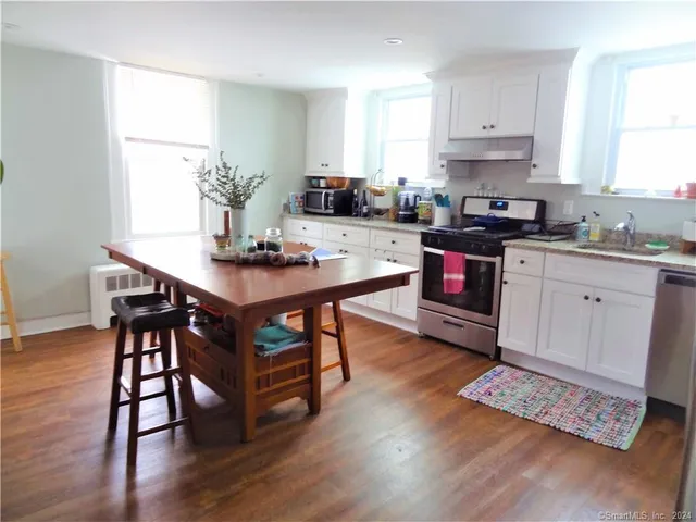 a kitchen with stainless steel appliances granite countertop a stove a sink dishwasher a microwave oven and a dining table with wooden floor