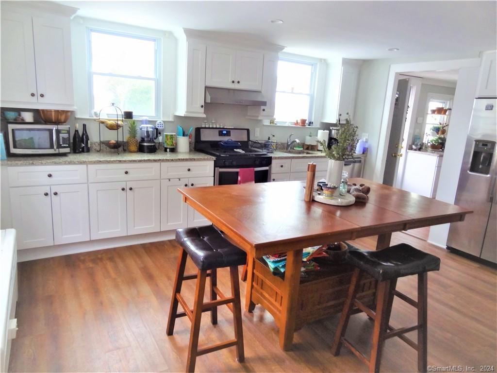237 Brewster Street Bridgeport, CT 06605 - Photo 3 of 23 a kitchen with stainless steel appliances granite countertop a stove a sink a microwave a dining table and chairs with wooden floor