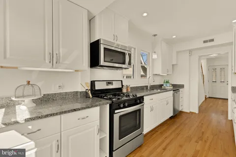 a kitchen with granite countertop a stove top oven a sink dishwasher and white cabinets with wooden floor