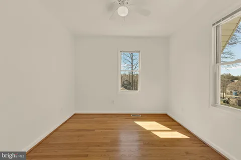a view of empty room with wooden floor and fan