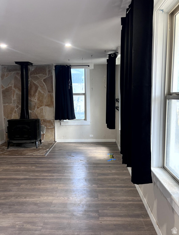 3161 Adams Avenue Ogden, UT 84403 - Photo 6 of 17 Room featuring a cast-iron stove with a stone surround, wood-finish flooring, recessed ceiling lighting, multiple windows, and light-toned walls