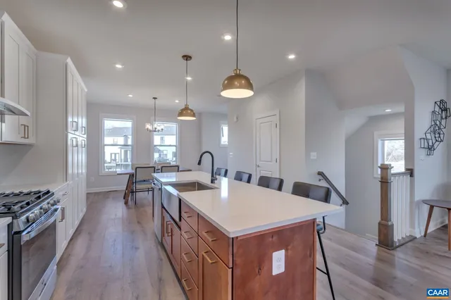 a kitchen with stainless steel appliances a stove a sink a refrigerator and a dining table with wooden floor