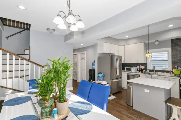 a kitchen with stainless steel appliances a chandelier a refrigerator a stove a sink a dining table and chairs with wooden floor