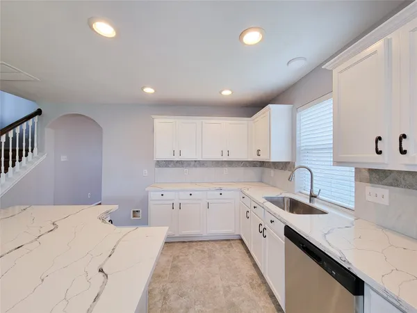 a kitchen with granite countertop a sink a stove a refrigerator and white cabinets with wooden floor