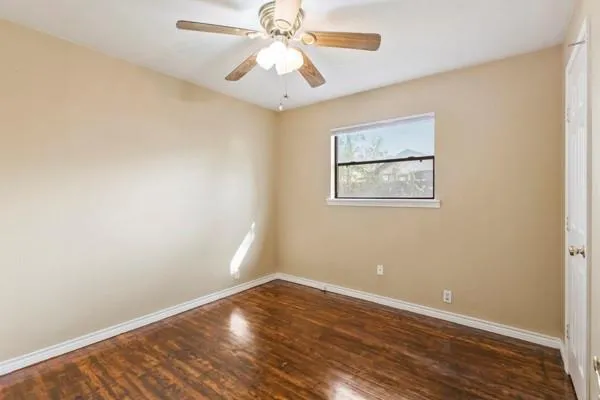 a view of an empty room with wooden floor and a ceiling fan