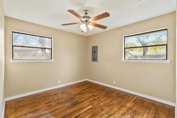 a view of an empty room with wooden floor and a ceiling fan