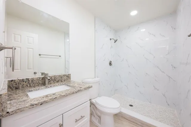 a bathroom with a granite countertop sink a toilet and shower