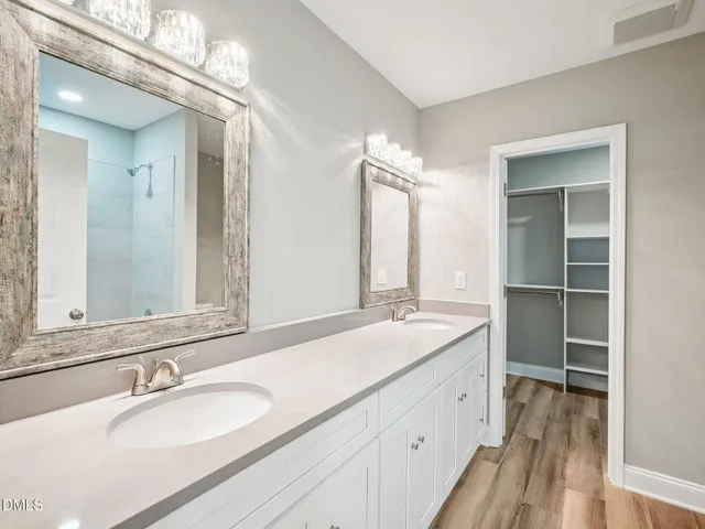 a bathroom with a granite countertop double vanity sink a mirror and a shower