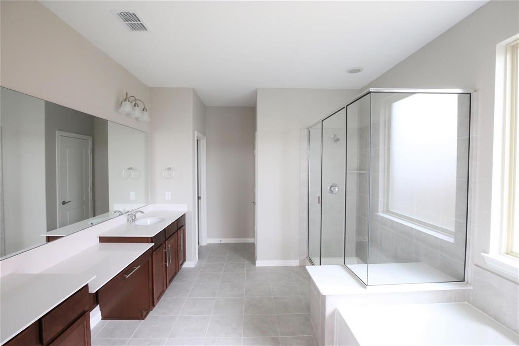 15142 Rosario Road Frisco, TX 75035 - Photo 11 of 21 Spacious bathroom featuring a dual vanity with white countertops and rich wood cabinetry, a large walk-in shower with glass enclosure, a separate soaking tub, and neutral tiled flooring